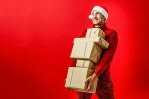 Portrait of one handsome new year man in red santa claus christmas hat with fur holding present box in studio on purple background, horizontal picture photo