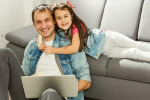 Bearded man and little girl at home family time sitting on floor on carpet browsing laptop together smiling joyful photo