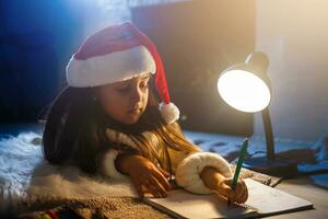 Little girl in Santa hat writes letter to Santa Claus near christmas tree and clock photo