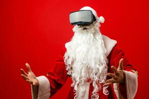 Papa Noel claus vistiendo virtual realidad gafas de protección, en un rojo antecedentes. Navidad foto