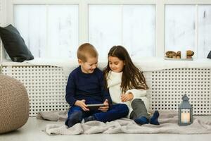 Two little kids sitting  boy girl with tablet computer, phone photo