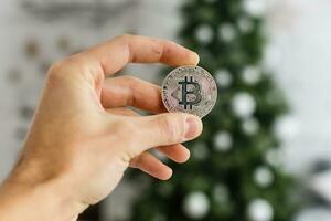 Man's hand holding silver bitcoin on Christmas lights bokeh background photo