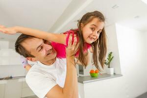 Little daughter and her handsome young dad are playing together in room. Girl is holding a toy plane and dad is holding his daughter photo