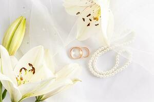 Top view of two gold wedding rings on a white bridal bridal veil and pearl beads. delicate white lilies. the concept of a wedding card, photo