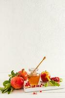 Beautiful still life with ripe pomegranates and apples, a bowl of honey. White background. The concept of Rosh Hashanah. A copy space. Vertical view. photo