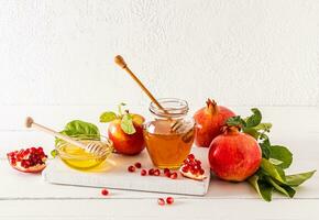 A composition of a jar and a bowl of different honey on a wooden board with ripe pomegranates and apples. wooden table. Roshhashan holiday. photo