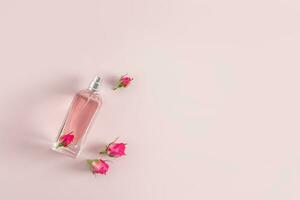 A beautiful bottle of women's perfume or spray on a pink background with small rosebuds. Top view. A copy space. Presentation of the fragrance. photo