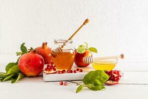 A jar and a bowl of delicious honey, ripe pomegranates and apples for the celebration of the Roshashan holiday. white background. front view. photo