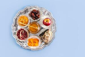 A silver plate with traditional treats for the Jewish New Year. The concept of the holiday of Rosh Hashanah. Top view. Blue background. copy space photo