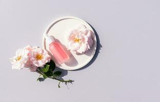 Cosmetic, serum in a white matte bottle for face and body skin care lies on a white plate. gray background. copy space. rose. top view photo