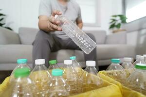 Home recycle eco green zero concept Man throwing empty plastic bottle in recycling bin with yellow garbage bags at home photo