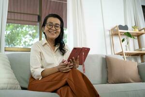 medio años asiático mujer participación célula teléfono. mayor mujer con inteligente teléfono. mayor mujer utilizando teléfono inteligente a hogar con tecnología concepto. foto