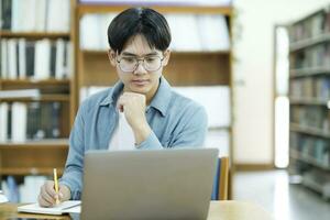 joven Universidad estudiante utilizando ordenador portátil para en línea aprendiendo, buscando y aprendizaje a biblioteca. foto