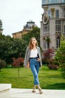 Girl with jacket on her shoulders stands on street. Architectural landmarks on background. Batumi city in Georgia. City walk. Girl wearing comfortable clothes, sneakers, jeans travels. photo