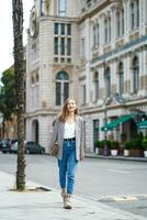 Smaling woman wallking on historic street Batumi city in Georgia. Young woman wearing jacket and jeans holding bag. In front of architectural buildings. Vertical composition. photo