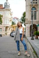 Girl threw jacket on her shoulder. Beautiful young woman wearing casual clothes standing on sidewalk. Historic building facade on background. City recreation. Person resting experiencing calmness photo