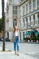 retrato de contento caucásico mujer con bolso caminando alrededor turístico ciudad y explorador calles arquitectura. hermosa mujer vistiendo chaqueta y pantalones wallking alrededor central ciudad de batumi en Georgia. foto