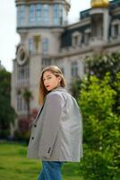 Womenswear, summer fashion. Rare view outdoor image of mysterious caucasian girl walking down city. Girl wearing jacket looking at camera over her shoulder. City walk in Historic District. photo