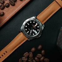 Surabaya, IDN, 2023 - Product photo of a luxury watch with a light brown synthetic leather strap, against a background of wood chips and coffee beans