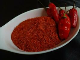 chile polvo es un Condimento mezcla de suelo chiles en un blanco cuenco con rojo chiles en un negro antecedentes. foto