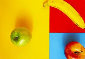 Red apple, green apple and banana on three colors background. Abstract background of fruits with creative design thinking. photo