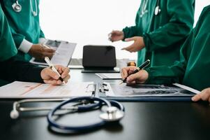 Medical team having a meeting with doctors in white lab coats and surgical scrubs seated at a table discussing a patients working online using computers in the medical industry photo