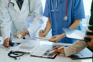 Medical team having a meeting with doctors in white lab coats and surgical scrubs seated at a desk discussing a patients working online using computers in the medical industry photo