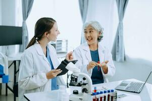 Two scientist or medical technician working, having a medical discuss meeting with an Asian senior female scientist supervisor in the laboratory with online reading, test samples and innovation photo