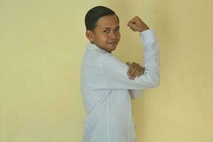 excited Asian man wearing white shirt showing strong gesture by raising arms and smiling proudly.  isolated on yellow background photo