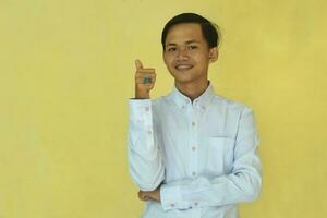 a man in a white shirt smiling happily giving a positive response with a thumbs up isolated on a yellow background photo