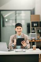 Young Asian business man working at office with laptop, tablet and taking notes on the paper. photo