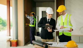 Contractor and architect looking at plan, tablet, laptop and talking about working on big project. Building in construction process photo