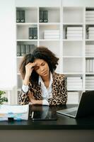 African Woman who is tired and overthinking from working with tablet and laptop at office. photo
