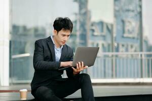 Young Asian business man working at outside business center with laptop, tablet, smartphone and taking notes on the paper. photo