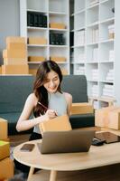 Startup small business SME, Entrepreneur owner woman using smartphone or tablet taking receive and checking online purchase shopping order to preparing pack product box. photo