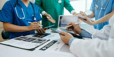 Medical team having a meeting with doctors in white lab coats and surgical scrubs seated at a table discussing a patients working online using computers in the medical industry photo