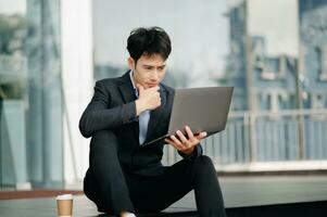 Young Asian business man working at outside business center with laptop, tablet, smartphone and taking notes on the paper. photo