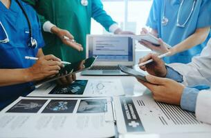 Medical team having a meeting with doctors in white lab coats and surgical scrubs seated at a table discussing a patients working online using computers in the medical industry photo