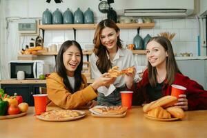 Group of friends making fun at home party.They sitting on desk in living room and eating pizza. happy photo