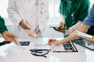 Medical team having a meeting with doctors in white lab coats and surgical scrubs seated at a desk discussing a patients working online using computers in the medical industry photo