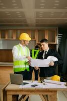 Contractor and architect looking at plan, tablet, laptop and talking about working on big project. Building in construction interior. photo