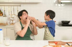 contento joven asiático padre y hijo comiendo sano comida en cocina a hogar foto