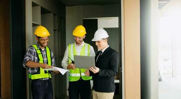 Contractor and architect looking at plan, tablet, laptop and talking about working on big project. Building in construction process photo