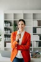 Confident business expert attractive smiling young woman typing laptop ang holding digital tablet on desk in office. photo