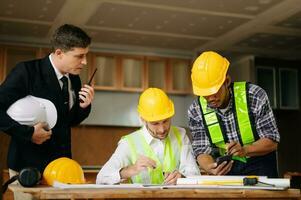 Contractor and architect looking at plan, tablet, laptop and talking about working on big project. Building in construction process photo