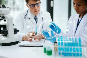 Focused mature male doctor and African female nurse look at tablet and laptop screen discuss anamnesis together. Concentrated diverse medical professionals photo