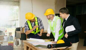 Contractor and architect looking at plan, tablet, laptop and talking about working on big project. Building in construction process photo