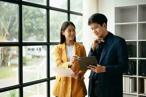 Two Asian business woman and man  discuss investment project working and planning strategy with tablet laptop computer in office. photo