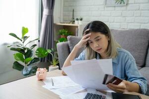 joven asiático mujer es estresado porque ella mira a muchos gastos cuentas y ella tiene No dinero a pagar a ellos. ella sensación muy grave deprimido. negocio financiero concepto. foto