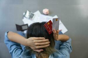 Top view of stressed young sitting Asian woman hands holding the head worry about find money to pay credit card debt and all loan bills. Financial problem concept. photo